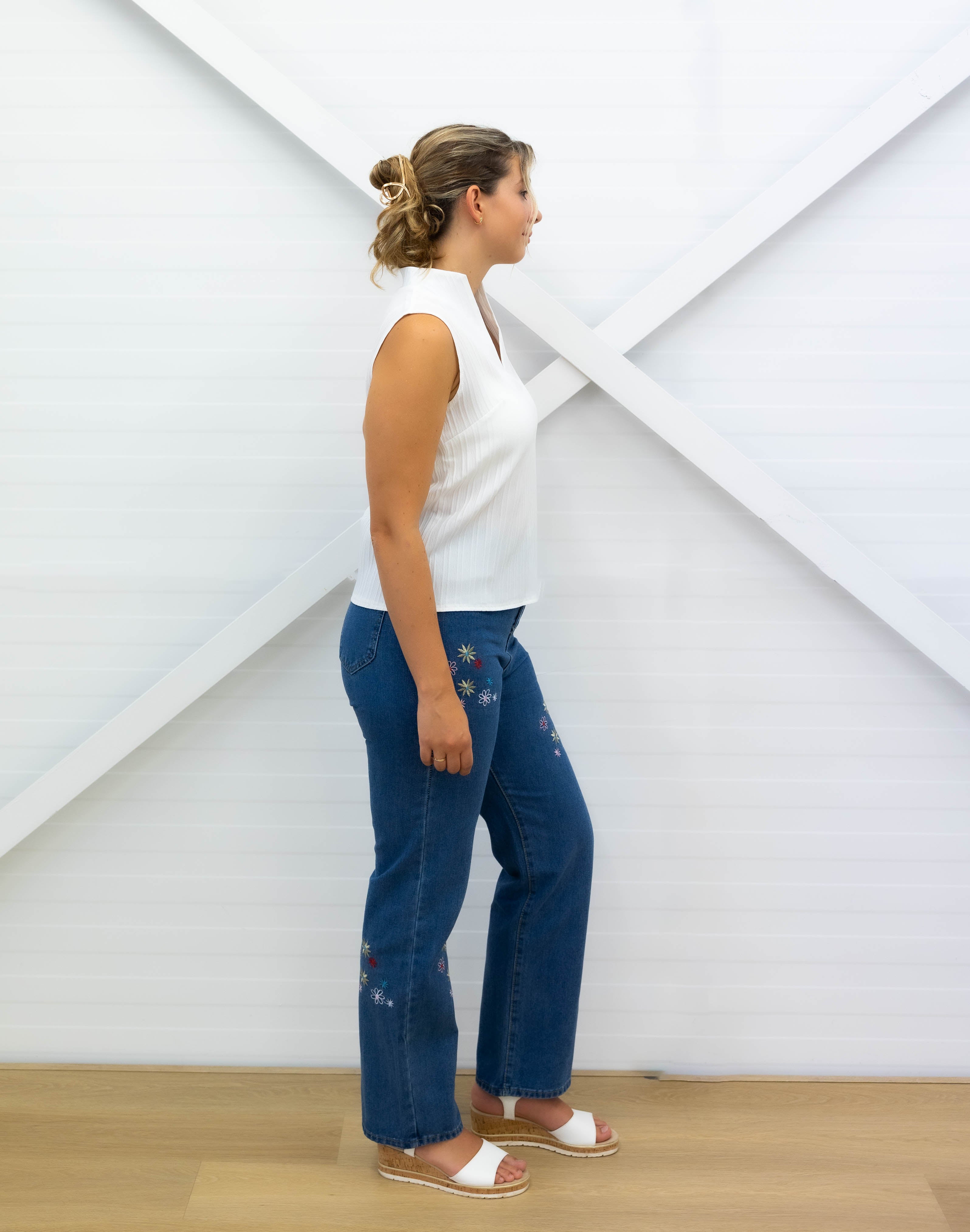 Woman wearing blue jeans and a white top against a white geometric-patterned wall.